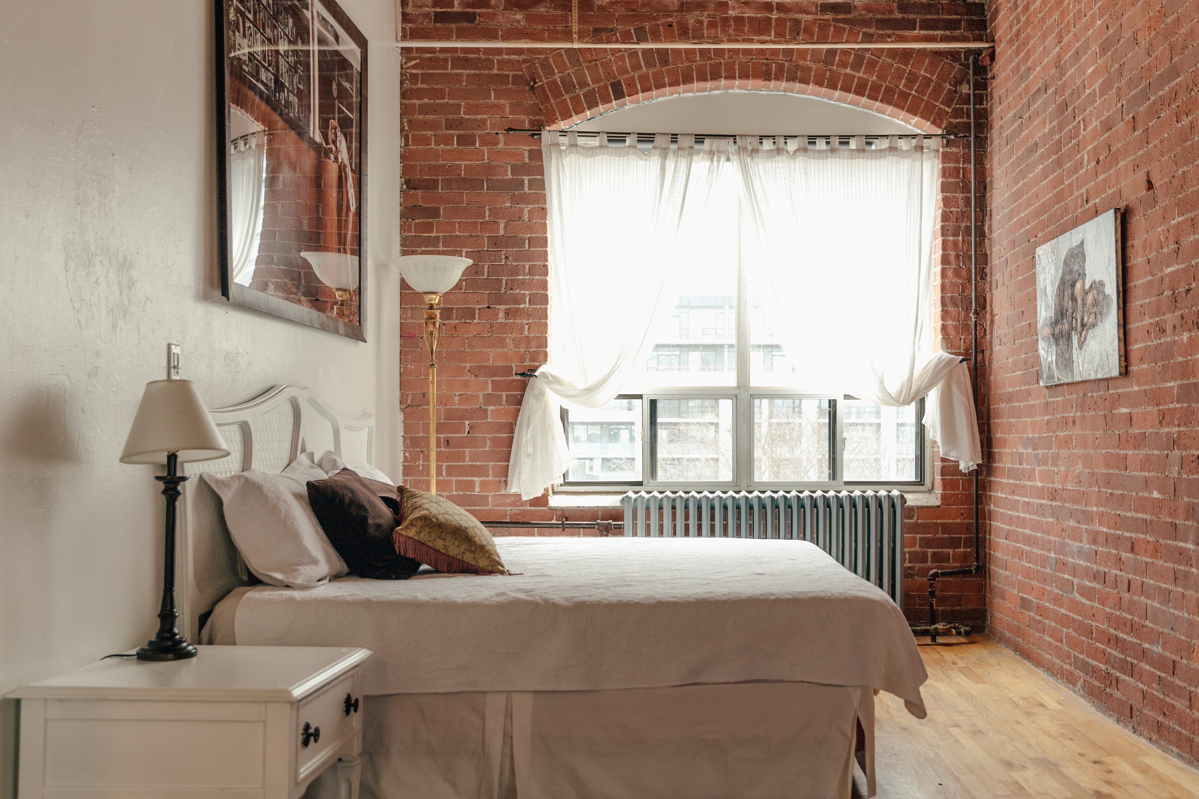 Foto de um dormitório, com cama de casal, mesa de cabeceira, abajours e quadros